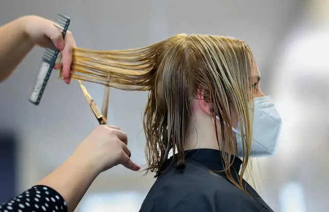 A hairstylist cutting a newly washed blond hair.